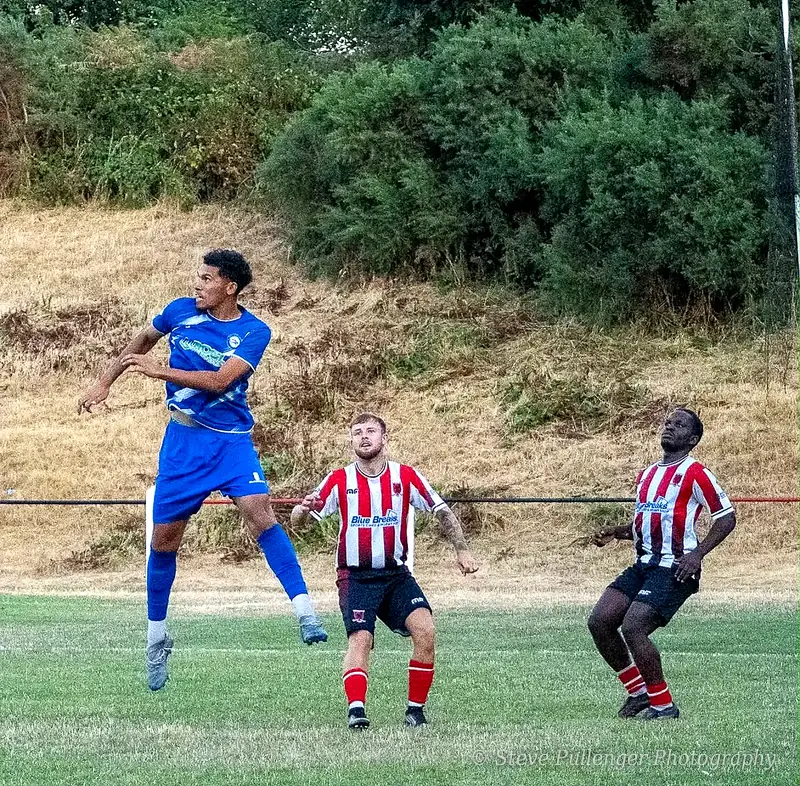 Footballer in blue leaping to head the ball as two defenders watch
